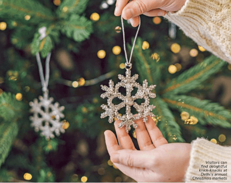 Hands holding a silver snowflake ornament in front of a lit Christmas tree